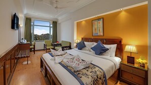 A hotel room with a large bed, a desk with a chair, a television, and a window with a view. - Hotel Baljees Regency (Shimla)