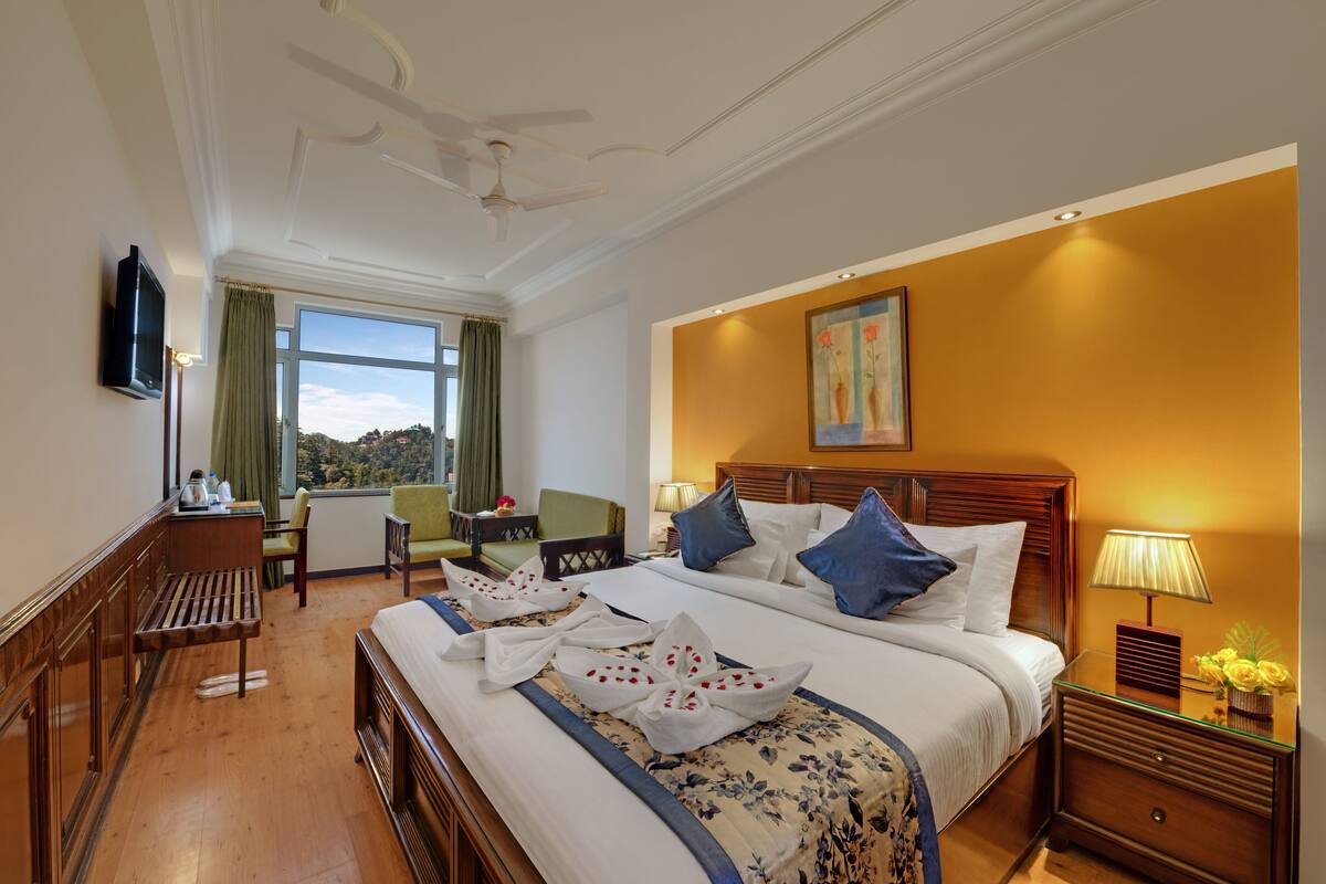 A hotel room with a large bed, a desk with a chair, a television, and a window with a view.