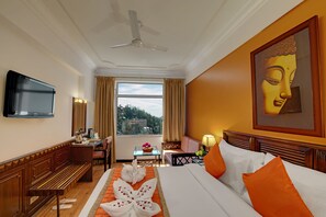 A hotel room with a bed, a desk, a chair, a television, and a window with curtains. - Hotel Baljees Regency (Shimla)
