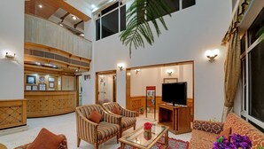 A spacious living area with a high ceiling, a television, and a coffee table. - Hotel Baljees Regency (Shimla)
