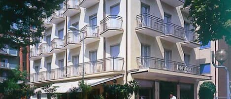 A multi-story hotel with balconies, a covered outdoor seating area, and a sign indicating it is a hotel.