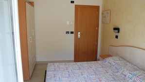 Ein Schlafzimmer mit Bett, Kleiderschrank, einer Tür und einem Wandlichtschalter.