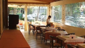 Ein Restaurant mit Holzbalkendecke, Tischen mit weißen Tischdecken und Stühlen.