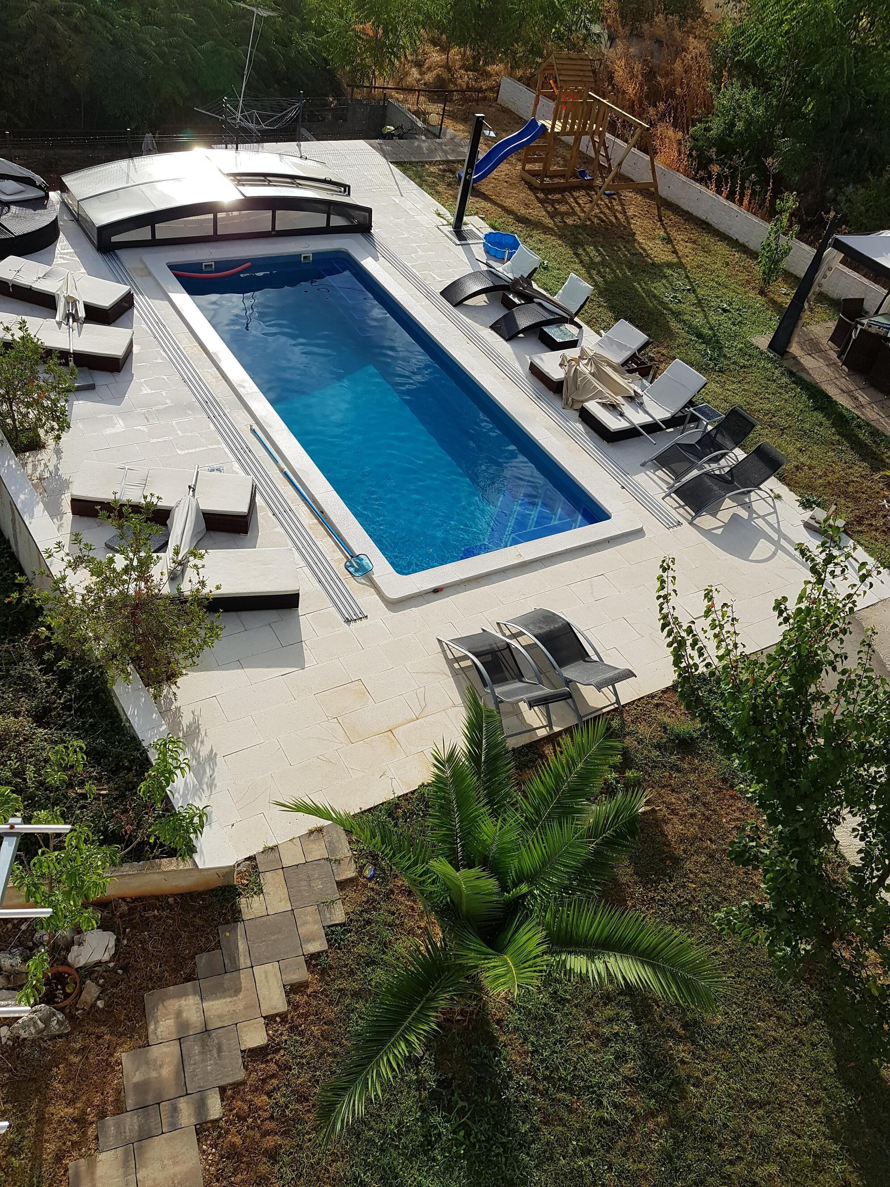 A rectangular swimming pool with a sunken seating area, surrounded by lounge chairs and a wooden play structure.