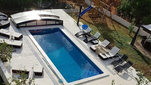 Une piscine rectangulaire dotée d’un espace salon en contrebas, entourée de chaises longues et d’une structure de jeu en bois.