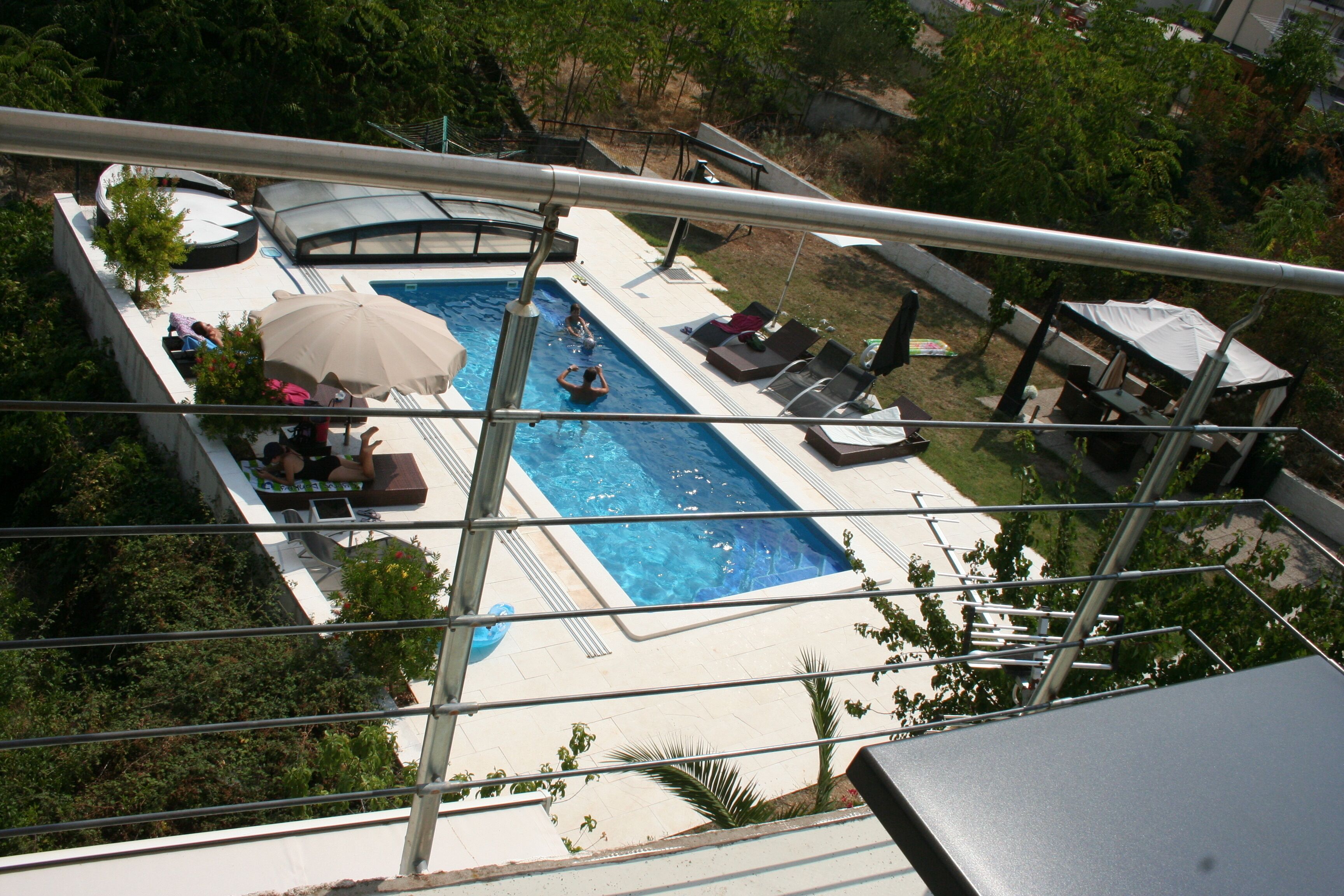 A rooftop pool with lounge chairs and umbrellas, surrounded by greenery.