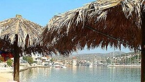 Une plage avec des parasols en chaume, d’où l’on peut admirer la mer et les bâtiments qui se dressent à l’arrière-plan.