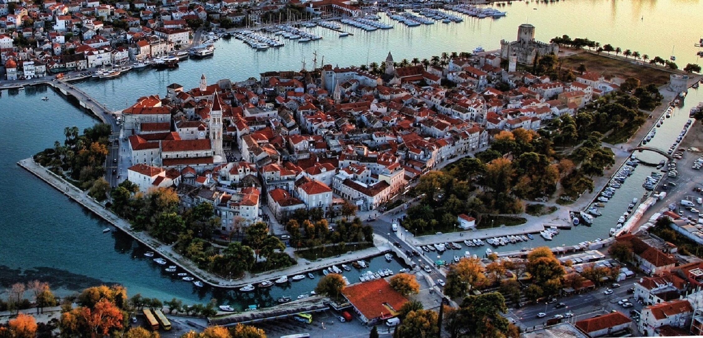An aerial view of a coastal town with a marina, historic buildings, and a prominent tower.