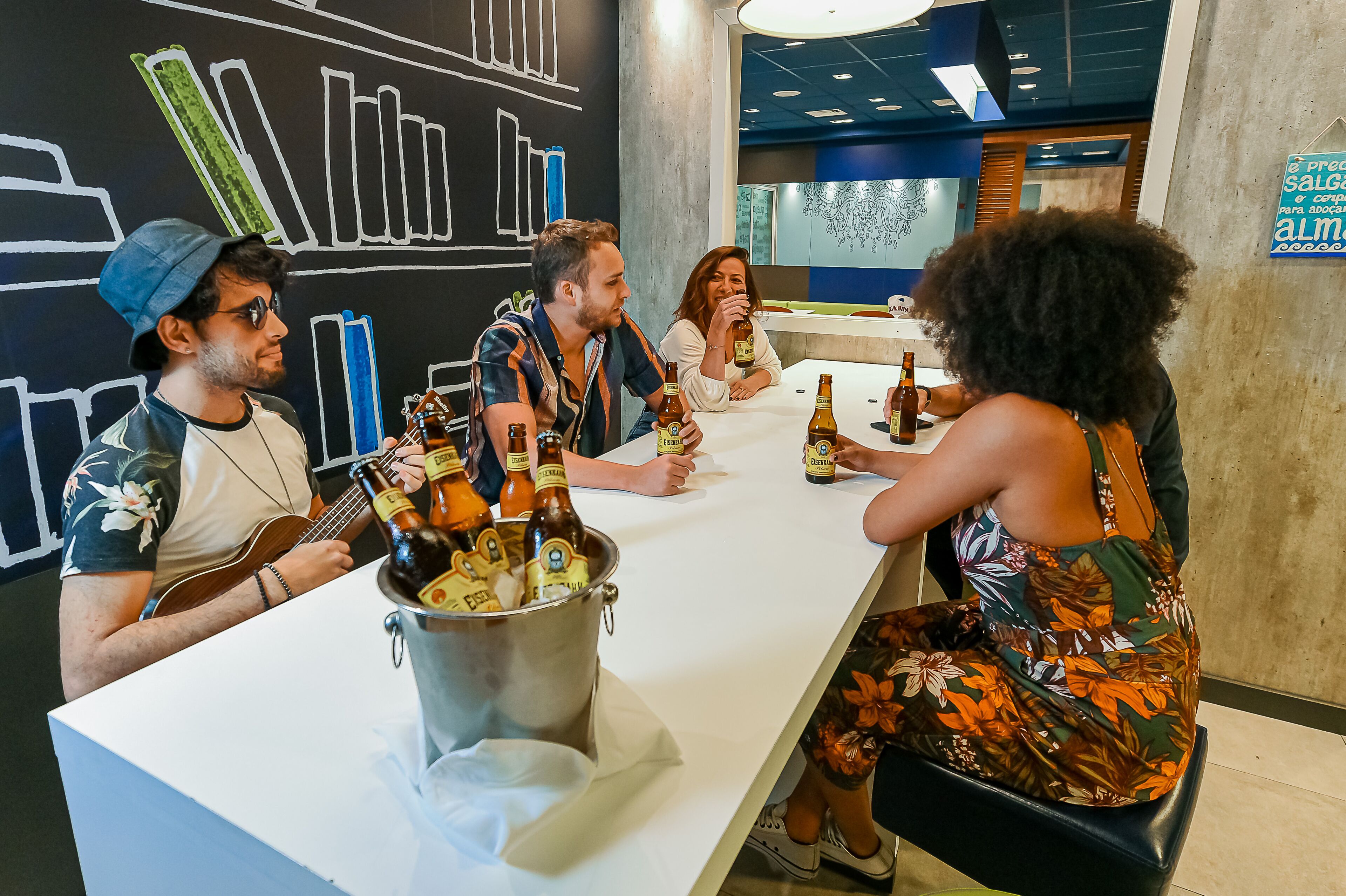 A group of people sitting around a table with a bucket of beer bottles.
