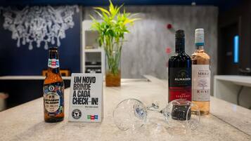 Una zona de bar con una botella de cerveza Stannis, una botella de vino Almodéen, una botella de rosado Mielo Seleção, y un letrero que dice 'UM NOVO BRINDE A CADA CHECK-IN'.