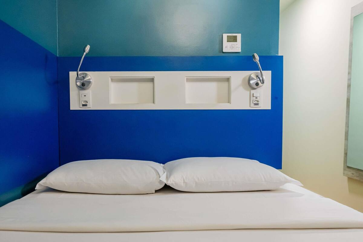 Een bed met witte beddengoed, een blauwe muur en een thermostaat aan de muur.