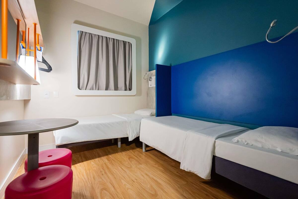Een kamer met twee eenpersoonsbedden, een tafeltje en twee rode krukken.