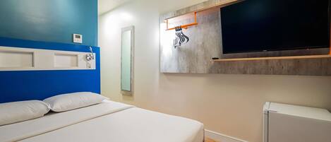 A hotel room with a bed, a wall-mounted TV, an air conditioning unit, and a small refrigerator.