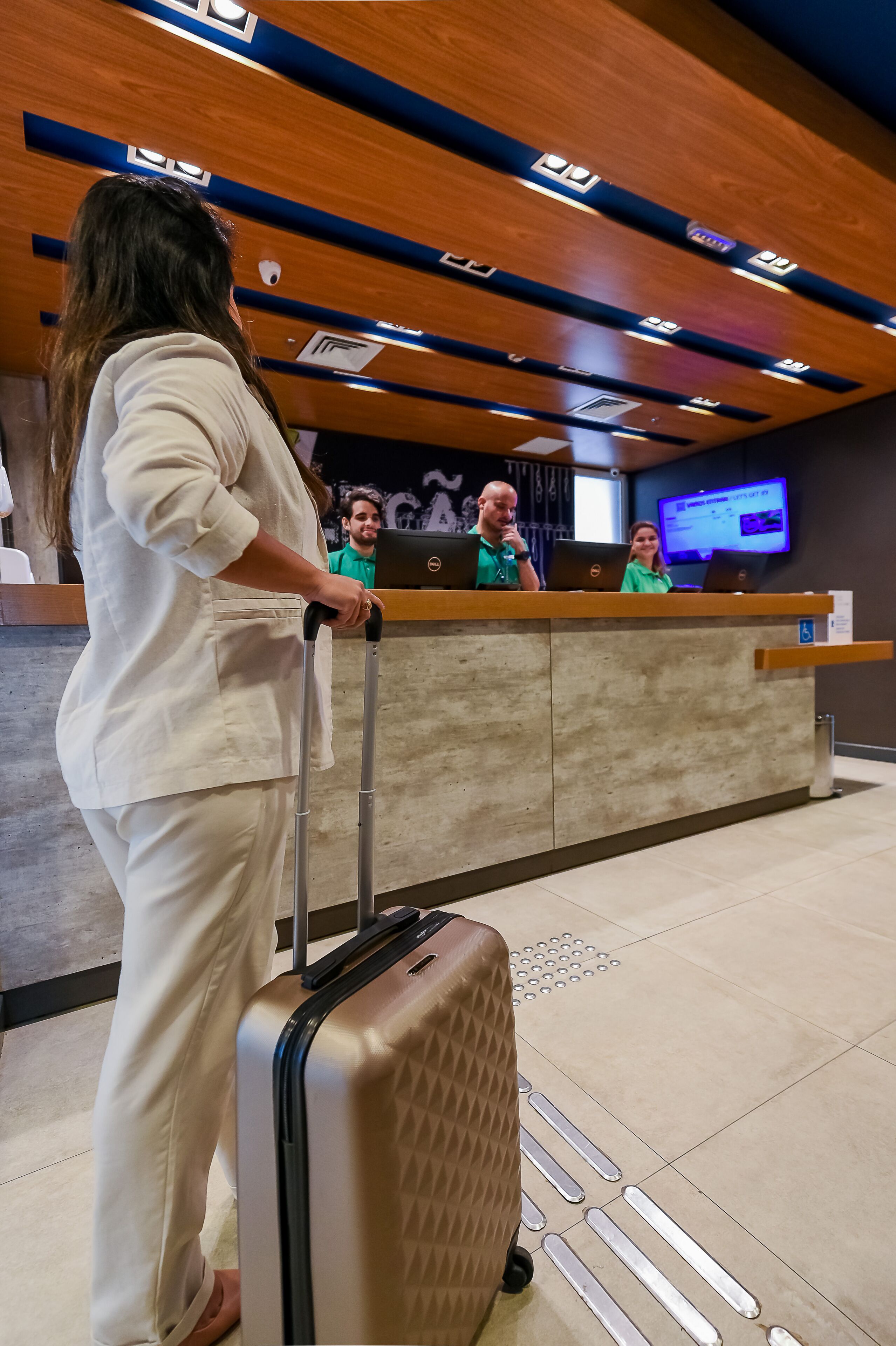 En hotellobby med ett träpanelat tak, en receptionsdisk och en digital skärm.