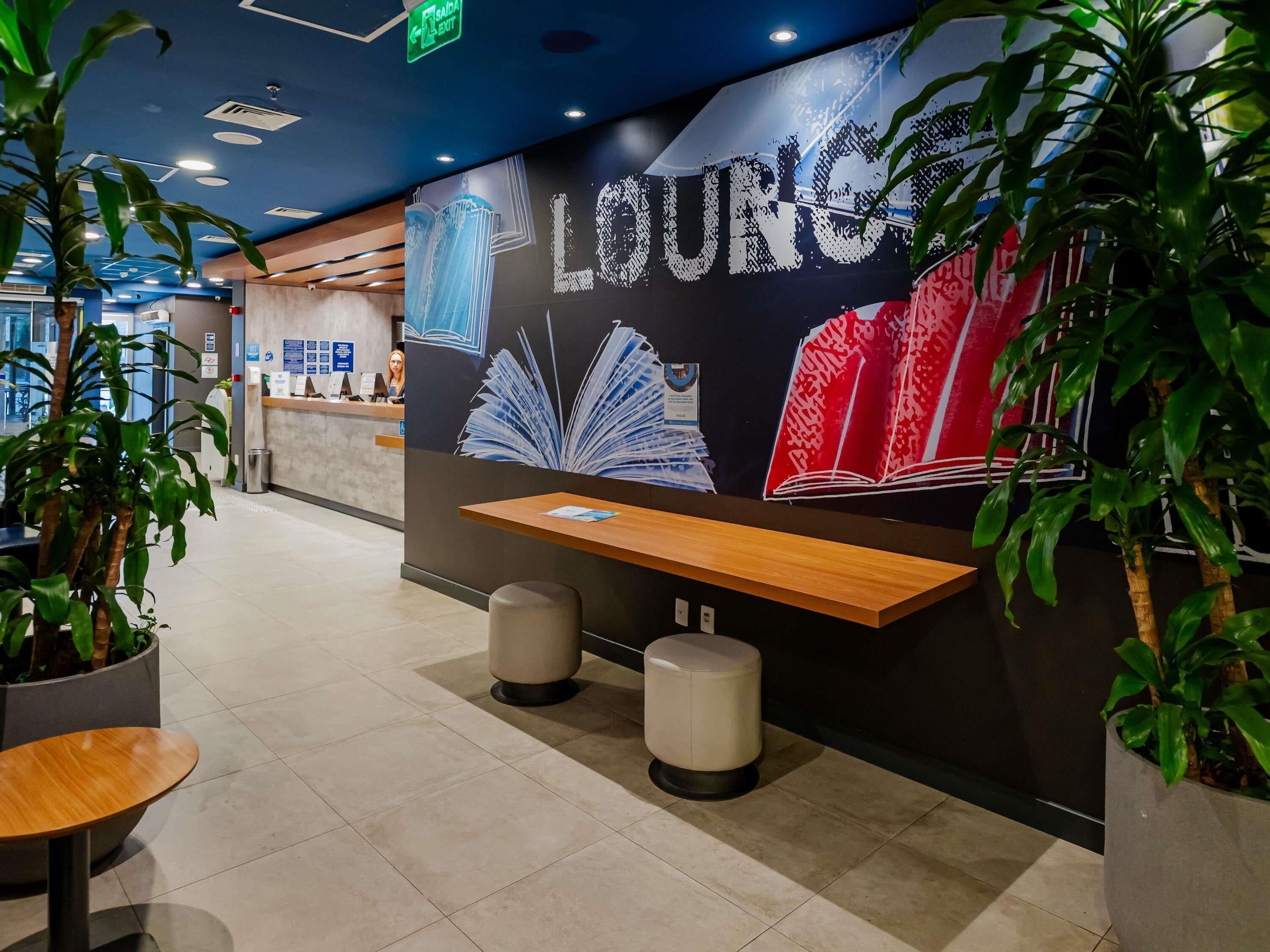 Un área de recepción con un mural en la pared, un mostrador de recepción, asientos y plantas en macetas.