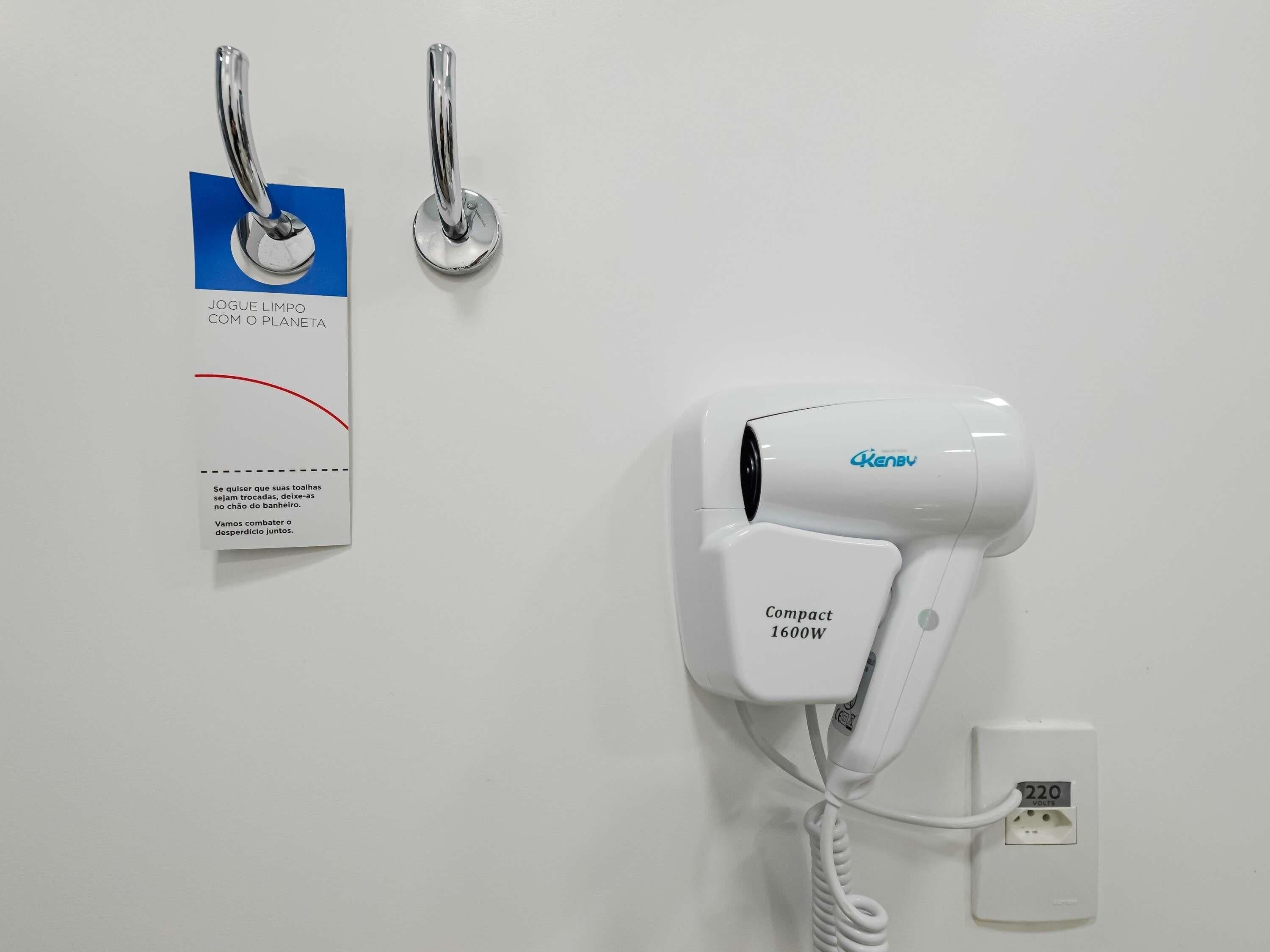 A hairdryer, a power outlet, and a tag with text on a white wall.