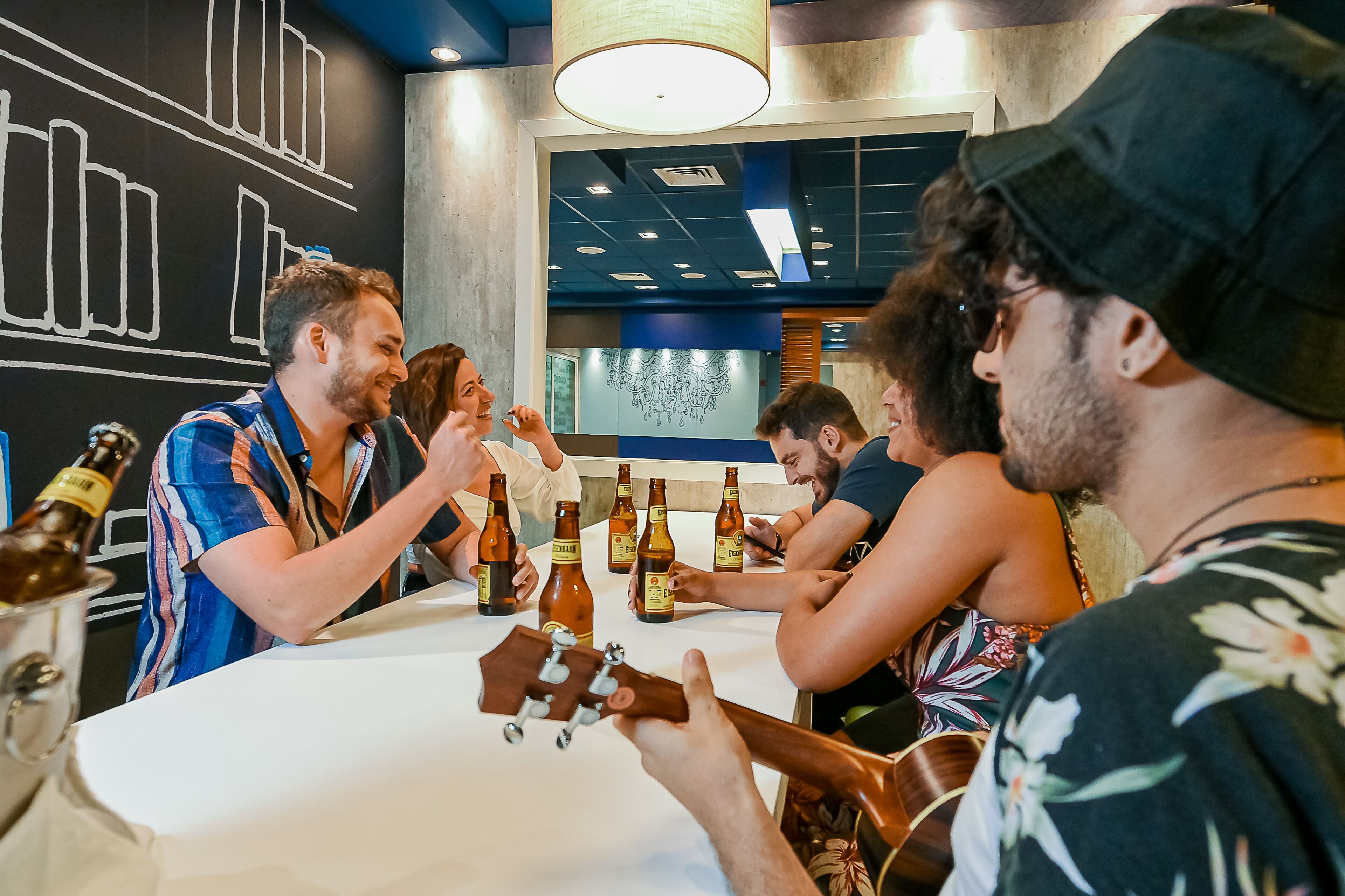 A group of people sitting around a table with bottles of beer, engaged in conversation.