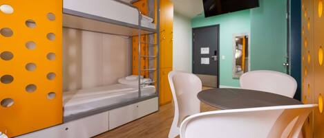 A bunk bed with a white mattress, a small table, and white chairs in a room with wooden flooring and a green accent wall.