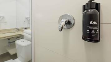 A bathroom with a white tiled wall, a chrome faucet, and a black bottle of Ibis shampoo.