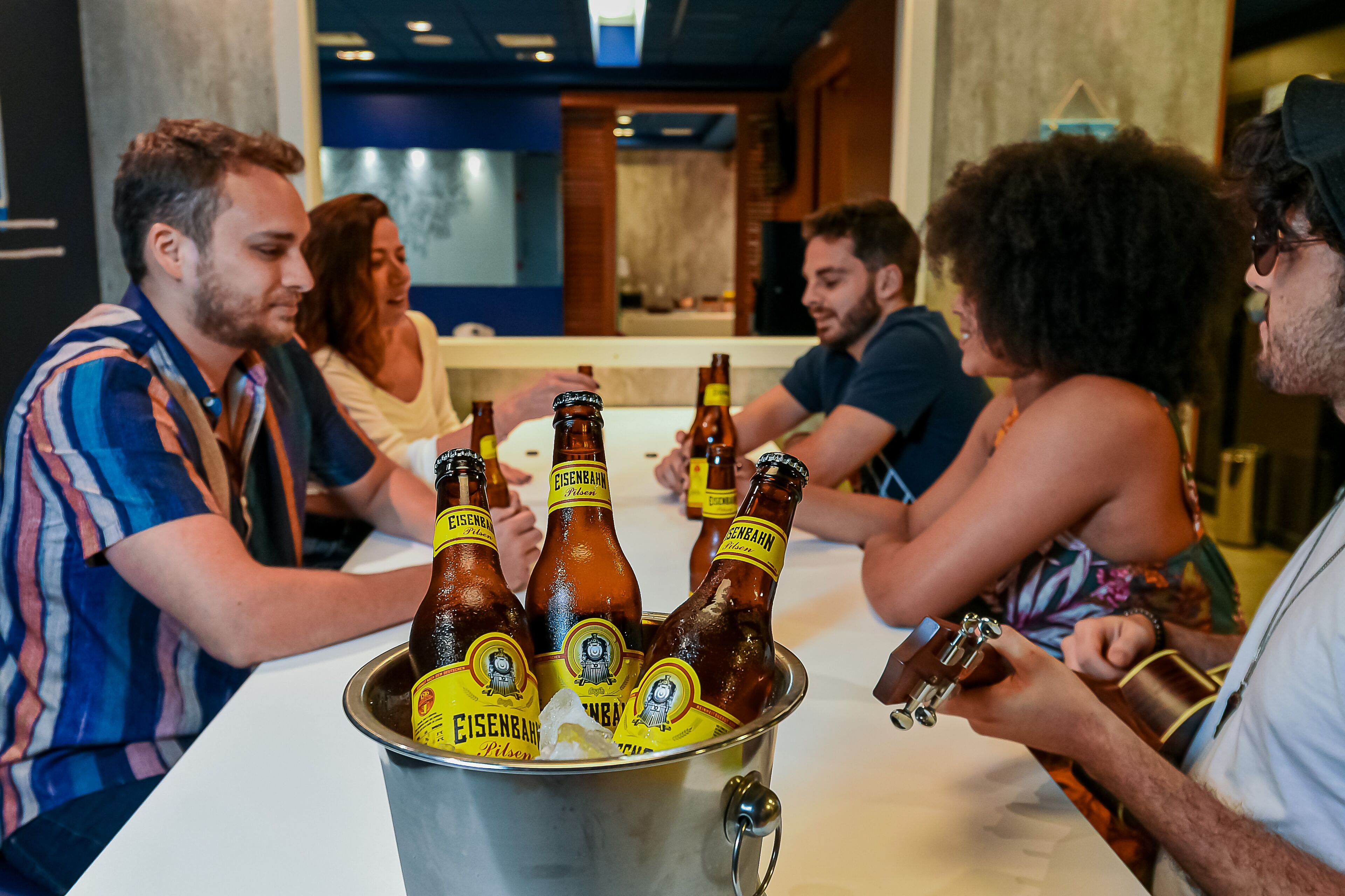 Un groupe de personnes est assis autour d’une table, devant un seau rempli de bouteilles de bière.