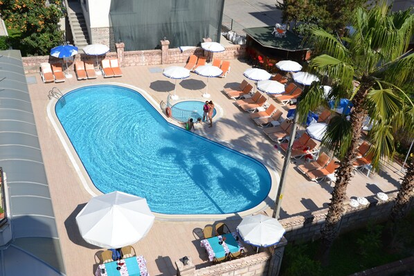 A swimming pool with lounge chairs and umbrellas, surrounded by palm trees and a stone wall.