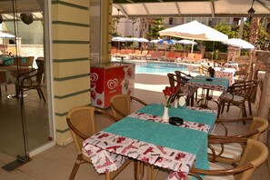 An outdoor seating area with tables and chairs, a pool, and umbrellas.