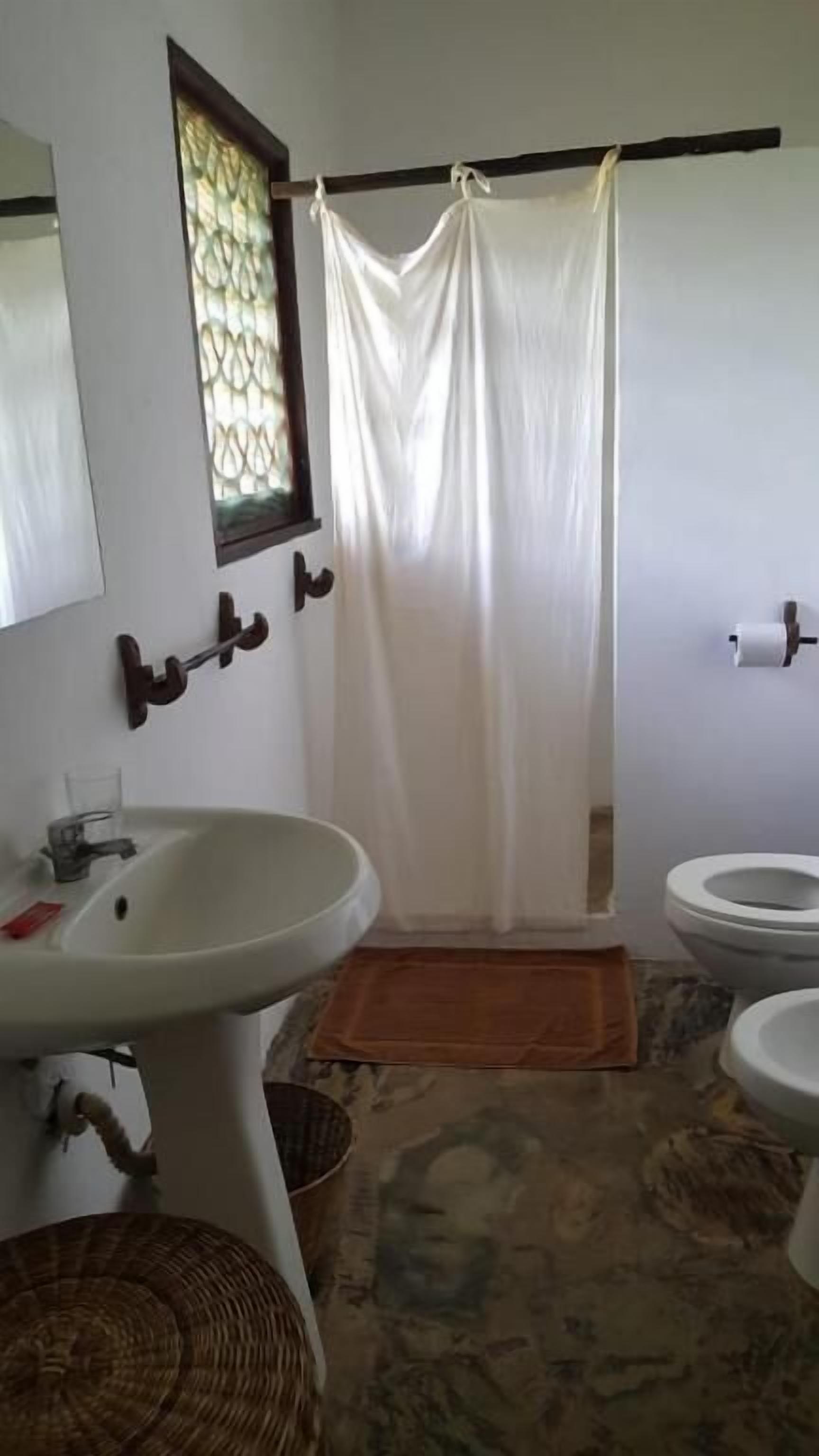 Un baño con cortina de ducha, dos lavamanos, un inodoro y una ventana con un diseño decorativo.