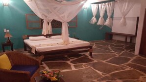 A bedroom with a bed, a chair, a nightstand, and a wall-mounted lamp. - Eco Villas Watamu (Watamu)