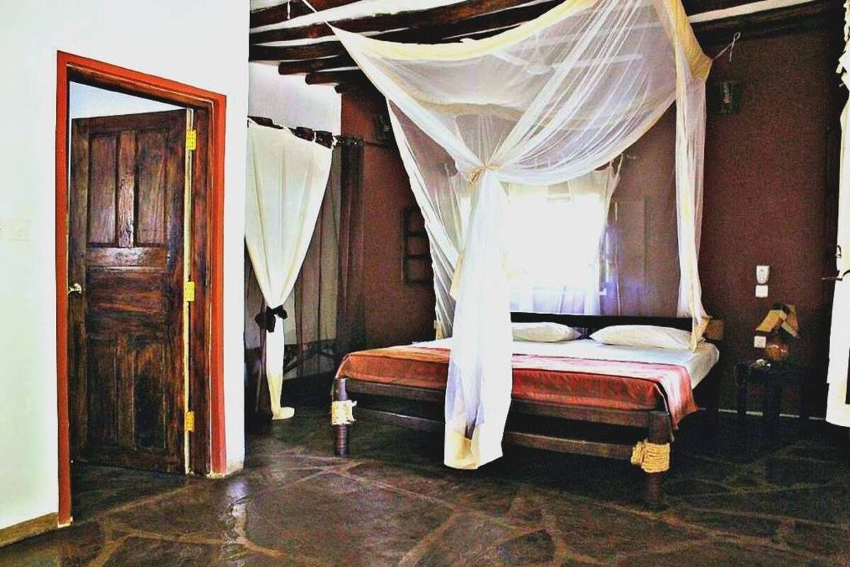 Una habitación con una cama bajo un dosel, una puerta de madera y un suelo de piedra.