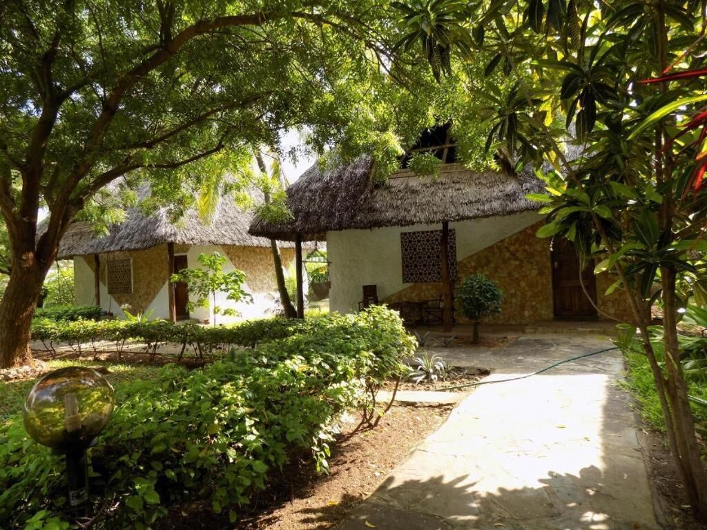 A courtyard with thatched-roof huts, surrounded by lush greenery and a clear pathway.
