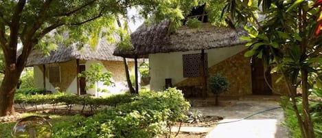 A courtyard with thatched-roof huts, surrounded by lush greenery and a clear pathway.
