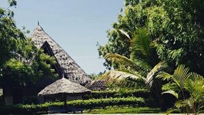A pool area with a thatched-roof structure and lush greenery. - Eco Villas Watamu (Watamu)