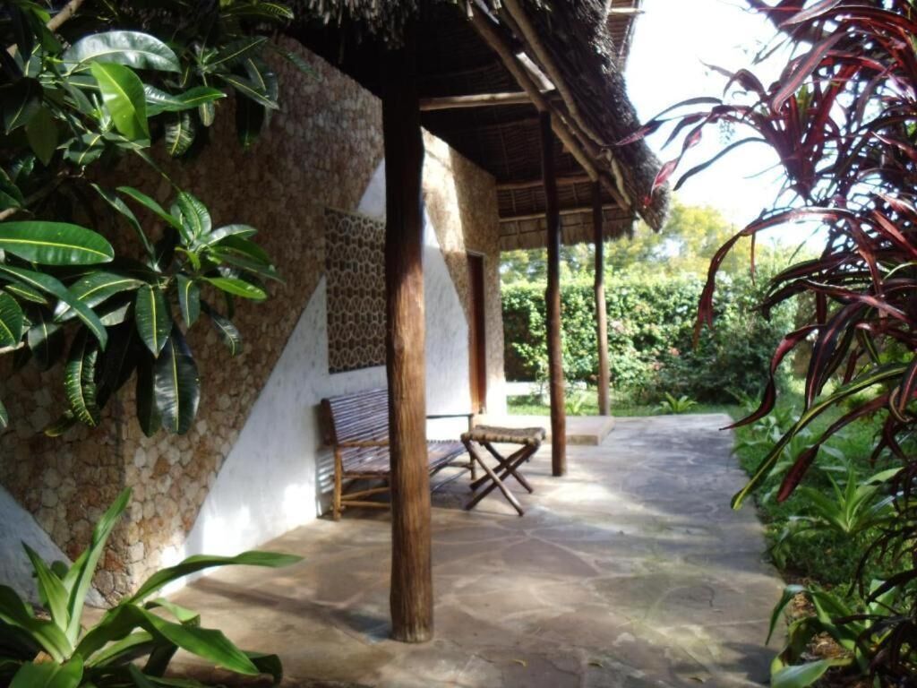 A covered outdoor area with stone flooring, wooden pillars, and a bench.