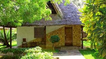 Una casa con techo de paja, un muro de piedra, una puerta de madera y un pequeño jardín con un banco y una planta en maceta.