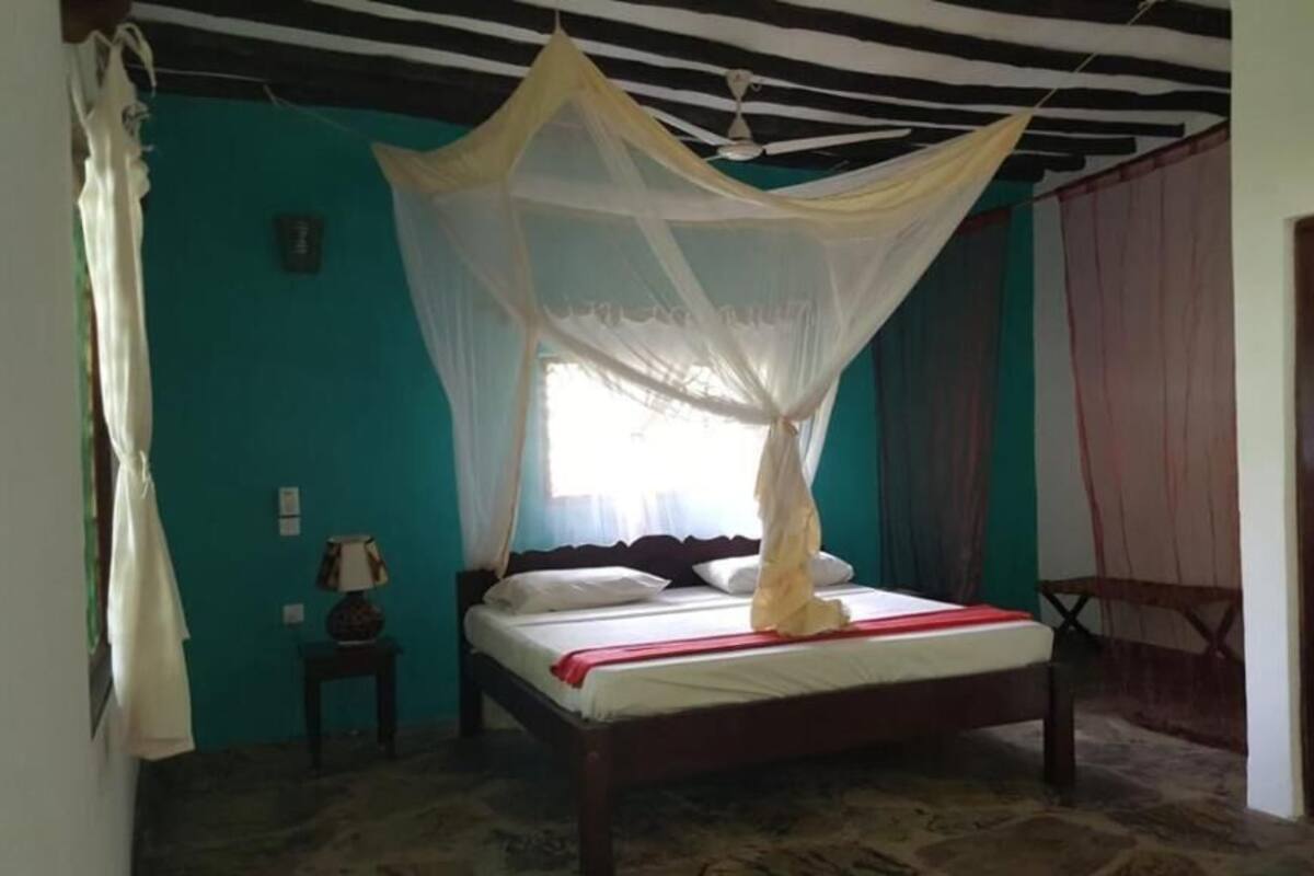 Una habitación con una cama, una mesita de noche, una ventana con cortinas y una puerta.