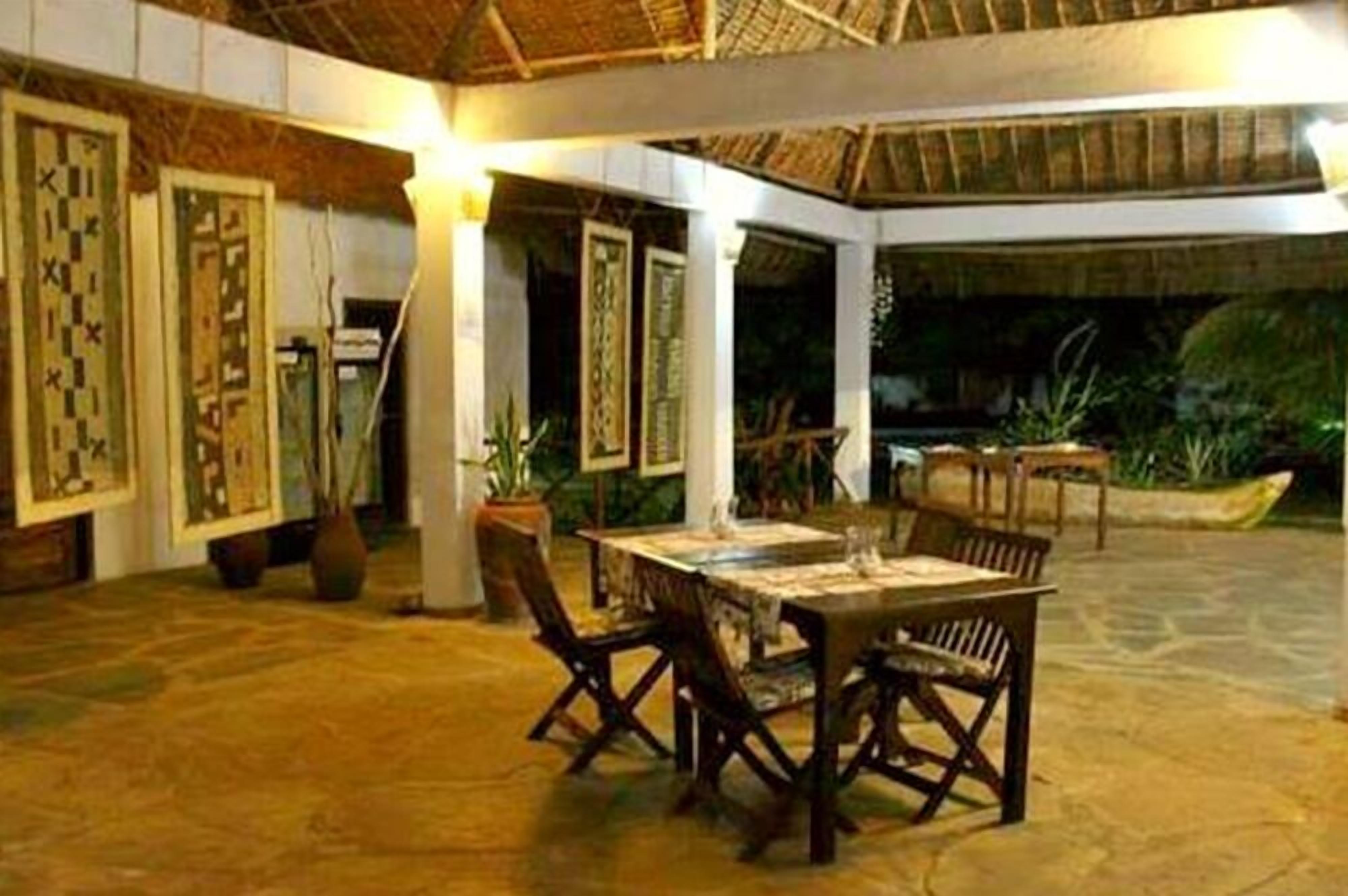 An indoor dining area with a thatched roof, wooden furniture, and framed artwork on the walls.