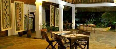 An indoor dining area with a thatched roof, wooden furniture, and framed artwork on the walls.