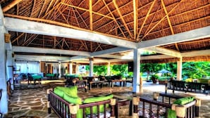 A covered outdoor seating area with stone flooring, wooden furniture, and a thatched roof. - Eco Villas Watamu (Watamu)