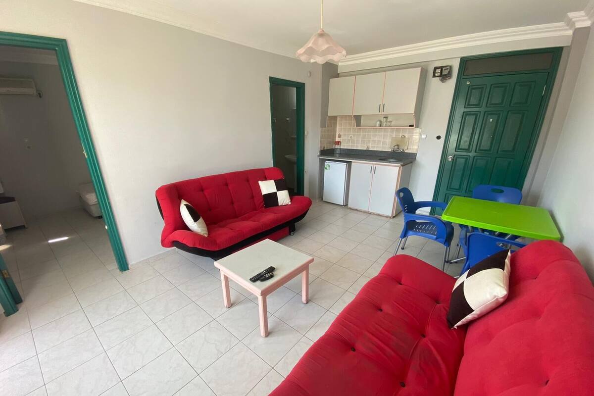 A compact living space with a red sofa, a small table, a kitchenette, and a green door.