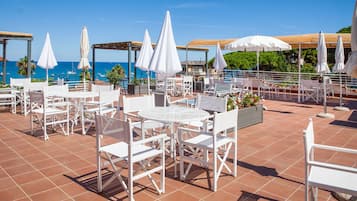 Een terras op het dak met witte tuinmeubels, parasols en uitzicht op zee.