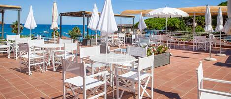 A rooftop terrace with white outdoor furniture, umbrellas, and a view of the sea.