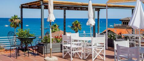 An outdoor patio with white furniture, a pergola, and a view of the sea.