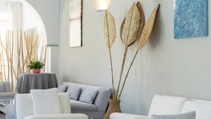 A modern living room with white sofas, a glass coffee table, and decorative elements like a vase with dried leaves and wall art.