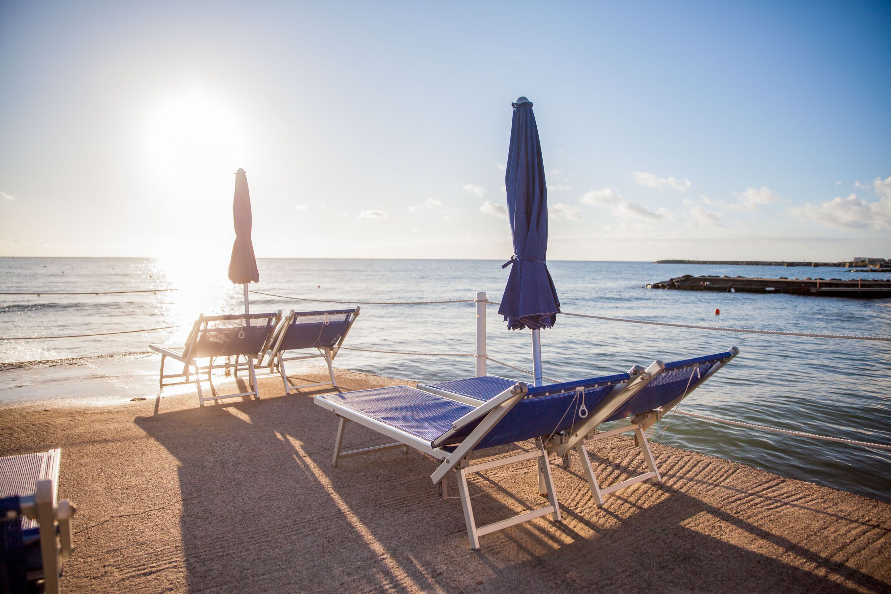 Une plage avec des chaises longues et des parasols, un ciel dégagé et une eau calme.