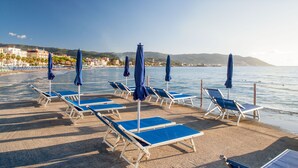 A beach with rows of blue sun loungers and umbrellas, a clear sky, and a calm sea.