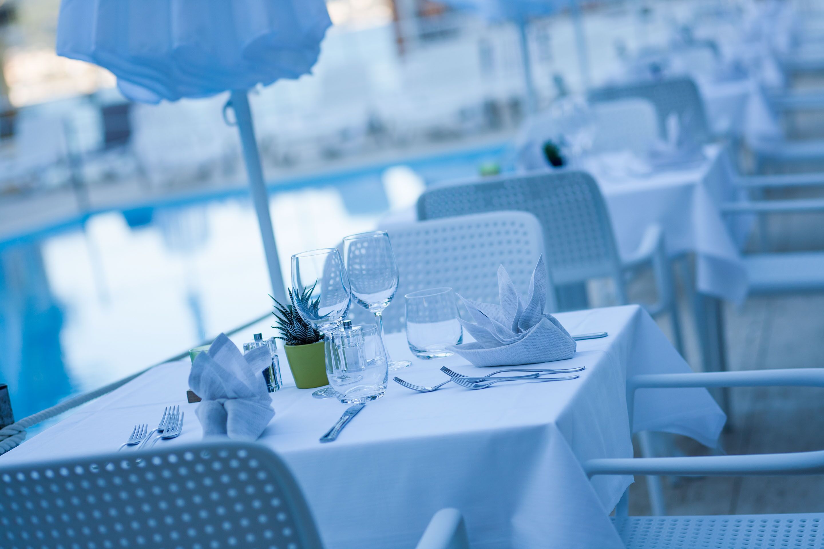 A dining area with tables set for two, near a pool.