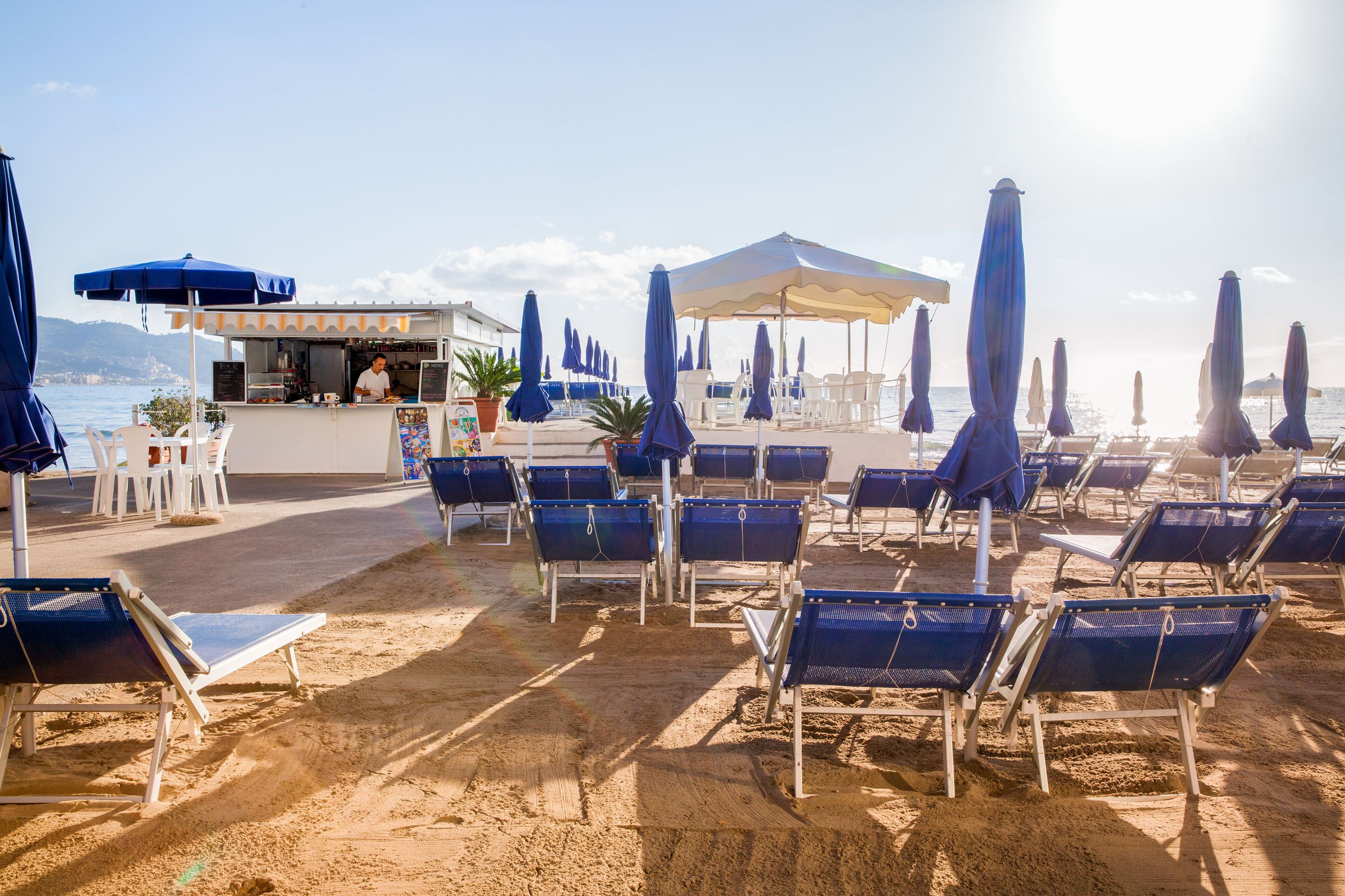 A beachside café with outdoor seating and umbrellas, overlooking the sea.