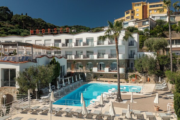 Un resort con piscina, sillas de descanso y vistas a una colina.