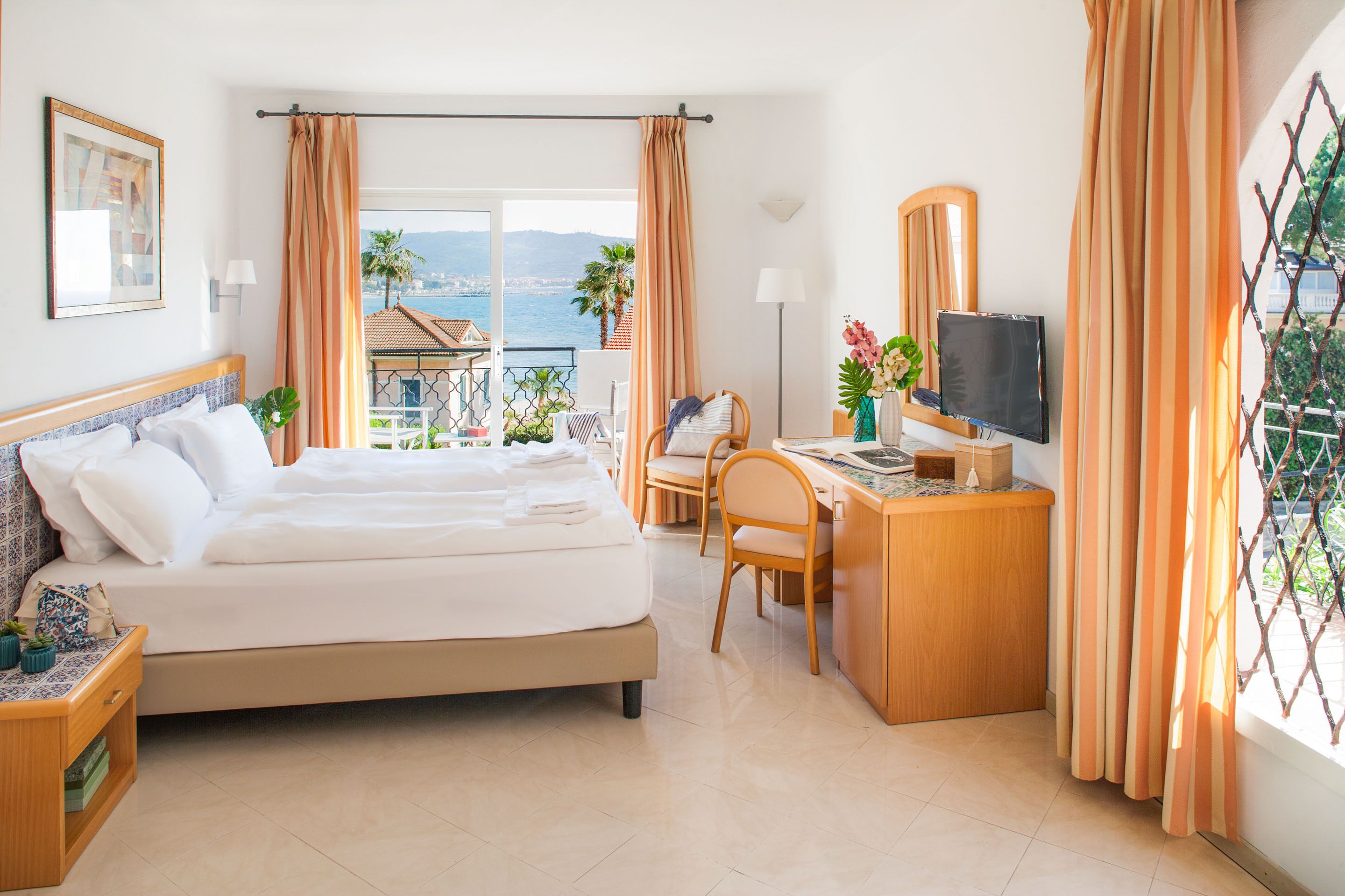 Une chambre d’hôtel équipée d’un lit, d’un bureau, d’une chaise, d’une télévision et d’un balcon avec vue sur la mer.