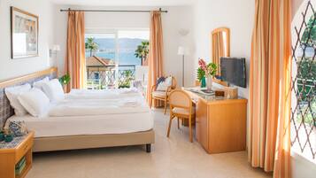 Ein Hotelzimmer mit Bett, Schreibtisch, Stuhl, Fernseher und einem Balkon mit Meerblick.